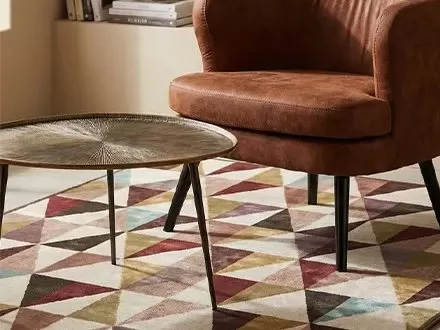 Poltrona in pelle color cuoio, tavolino in metallo bronzato e tappeto a triangoli colorati in un soggiorno